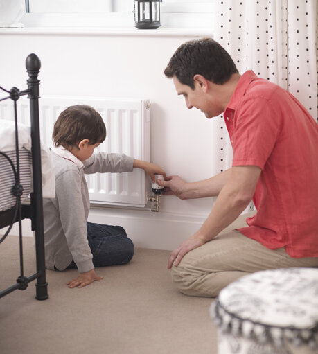 Father teaching son to adjust thermostat on radiator in bedroom of energy efficient house