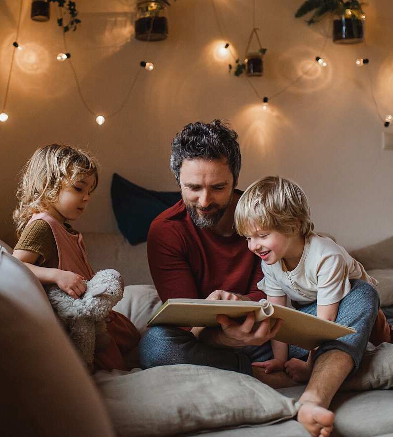 Mature father with two small children resting indoors at home, looking at photo album.