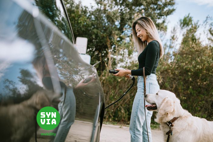 Woman With Dog Plugs In Electric Vehicle to Charge
