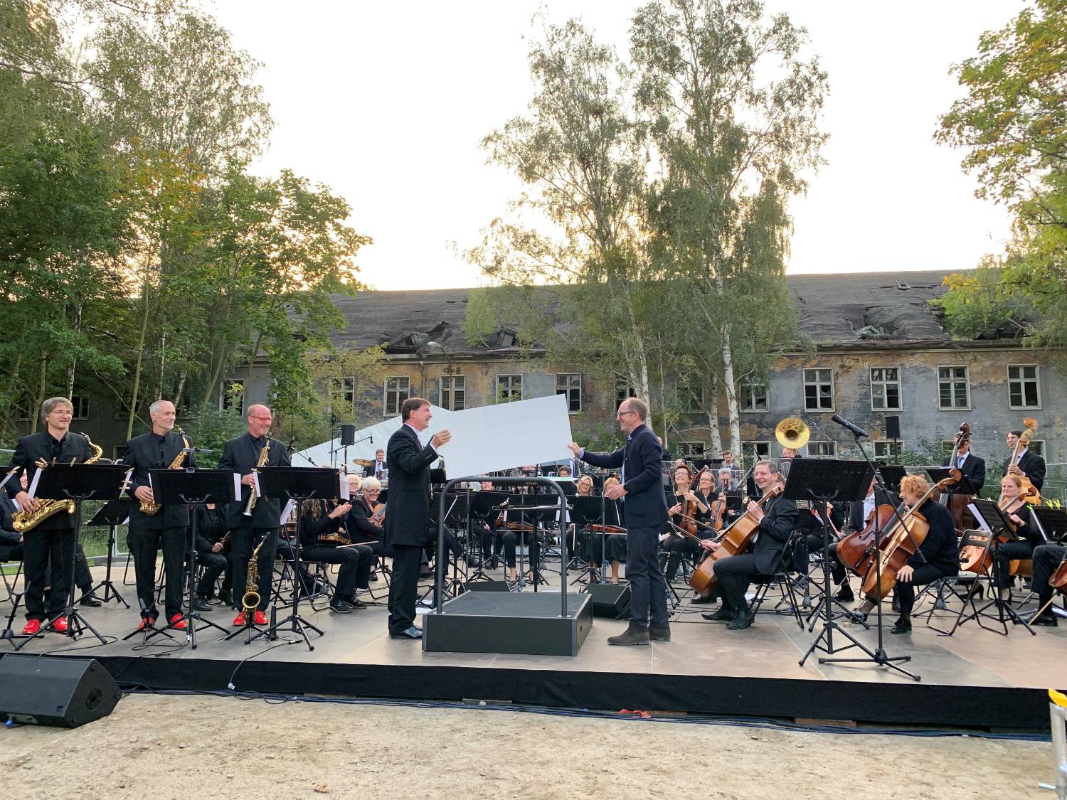 Ein Orchester musiziert zusammen draußen vor einem maroden Gebäude.