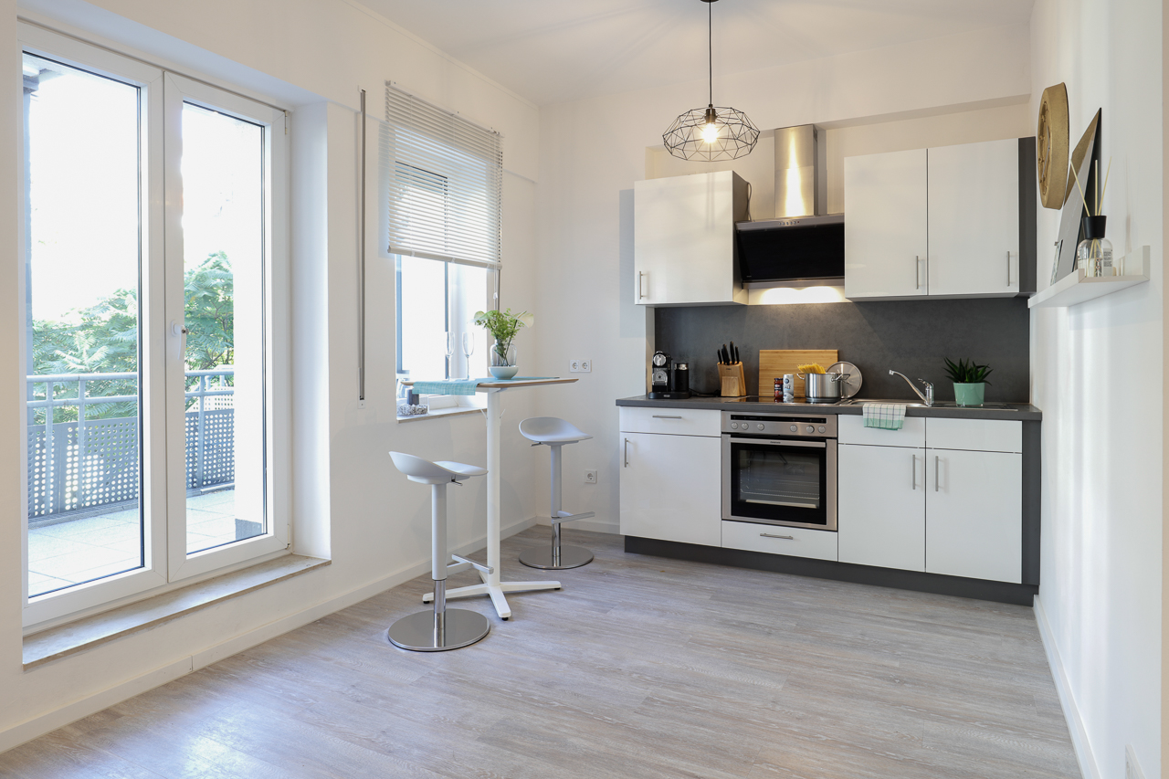 Moderne weiße Küche mit Barhockern neben Balkonfenstern.